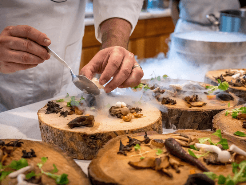 Chef-kok bereidt een gastronomisch gerecht met rook en bijzondere ingrediënten op houten serveerplanken.